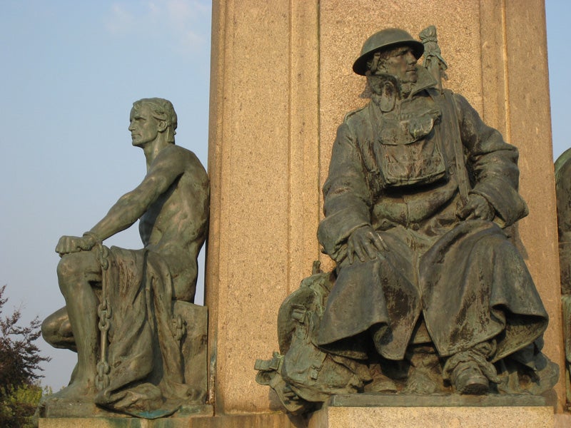 Bronze statues of a seated man and woman flanking a stone column, with the focus on the details and patina of the sculptures under natural lighting.