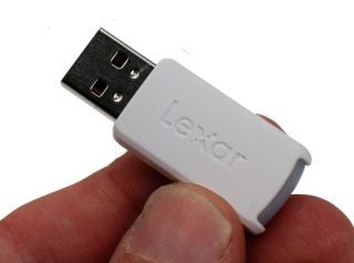 Close-up of a hand holding a white Lexar JumpDrive FireFly USB flash drive with black USB connector visible.