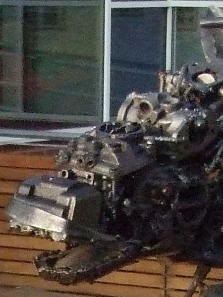 Blurred image of a mechanical or electronic device with intricate parts, possibly a disassembled engine or machinery, sitting on a wooden surface with a glass window in the background.