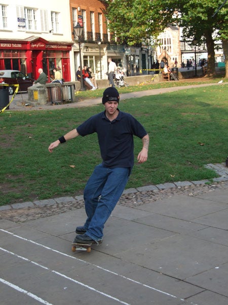 Man skateboarding in a public square captured in daylight with Fujifilm FinePix S6500fd camera.
