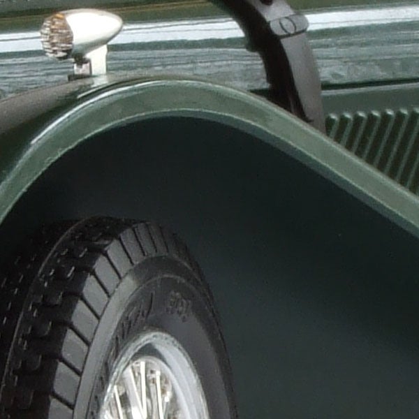 Close-up of a classic car's green fender and wheel with chrome details and white sidewall tire.