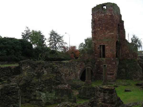 Photograph of an old brick tower ruin with arched doorway, surrounded by greenery, under an overcast sky.