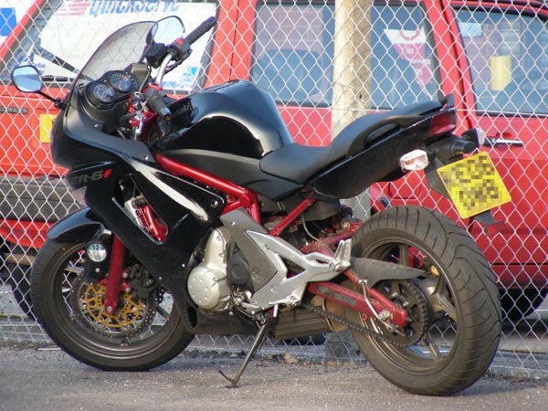 Sharp photo of a black and red sport motorcycle parked in front of a chain-link fence with a checkered pattern behind it, demonstrating the image quality of the Nikon Coolpix S10 camera.