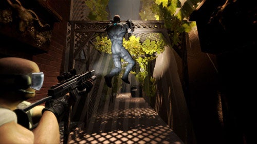 A screenshot from the video game Splinter Cell: Double Agent showing a third-person perspective of the protagonist climbing a fence in a stealth mission while an enemy soldier with a gun prepares to aim in the foreground.