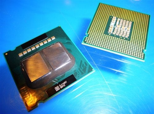 Intel Core 2 Extreme QX6700 processor with heatspreader facing up next to its underside showing pins, on a metallic surface.