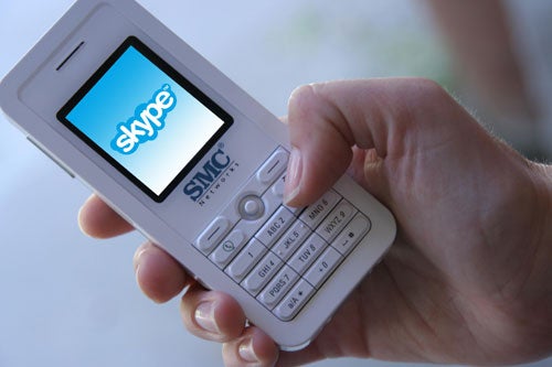 A hand holding the SMC WSKP100 Skype Phone with the screen showing the Skype logo and the phone's keypad visible.
