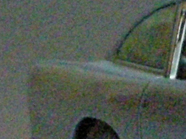Blurry low-light image showing indistinct shapes and colors with visible digital noise, possibly demonstrating the Nikon Coolpix S7c's performance in low-light conditions without flash.