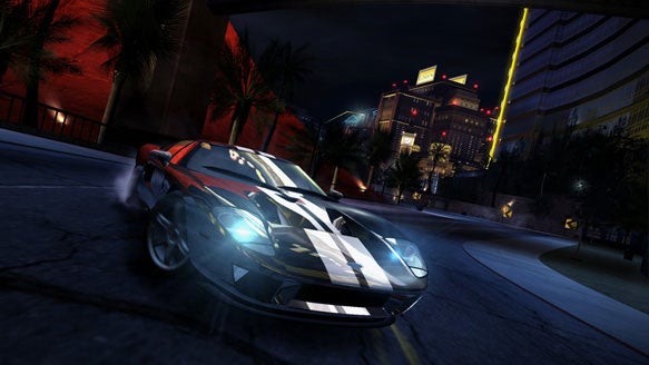Screenshot of the video game Need for Speed: Carbon depicting a racing car with a black and white design drifting around a corner at night with city buildings in the background.