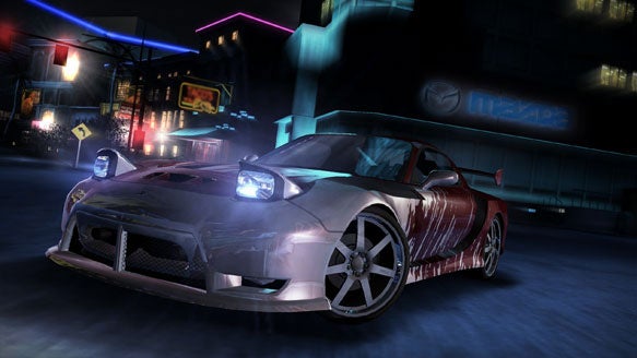 In-game screenshot from Need for Speed: Carbon showing a customized sports car racing through a neon-lit city street at night.