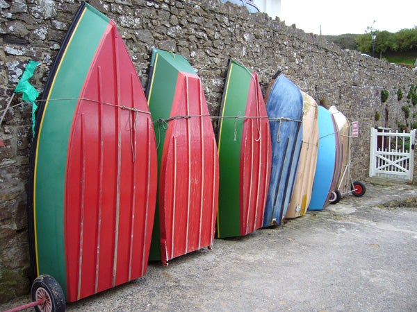 Assorted colorful boats standing upright against a stone wall.
