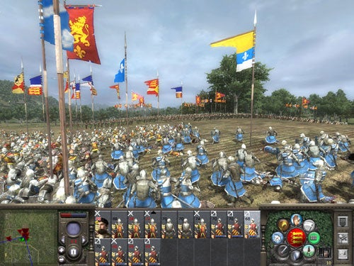 Screenshot from the video game Medieval 2: Total War showing a battle scene with knights in armor and various colorful banners waving above the battlefield, including the game's user interface at the bottom showcasing unit selections and command options.