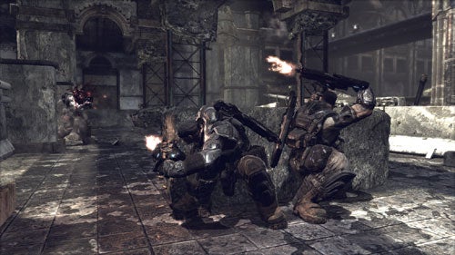 A screenshot from the video game Gears of War showing two characters in combat armor taking cover behind a stone block and firing at enemies in a dilapidated urban environment.