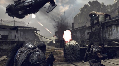 Screenshot from the Gears of War video game showing two characters taking cover behind rocks with a helicopter flying overhead in a desolate, war-torn landscape.
