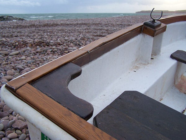 A close-up image of a boat's interior edge with wooden detailing, photographed with the Kodak EasyShare Z710, showcasing the camera's detail capture ability. The background is blurred with visible pebbles and a stormy sea, indicating the camera's shallow depth of field feature.