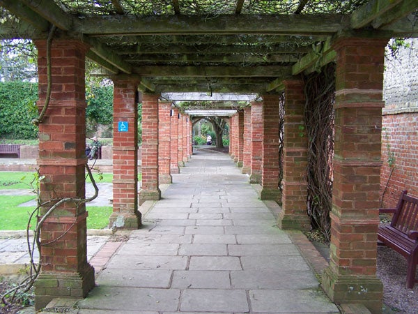 A brick pergola walkway with a tiled pavement, climbing plants, and benches in what appears to be a peaceful garden setting, potentially captured with a Kodak EasyShare Z710 camera.