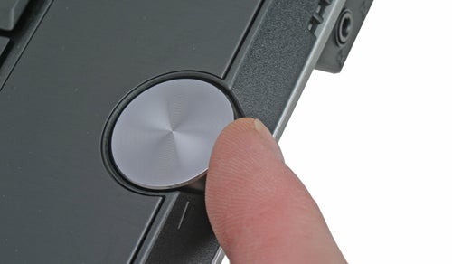 Close-up of a person's finger pressing the power button on a Toshiba Qosmio G30-102 laptop.