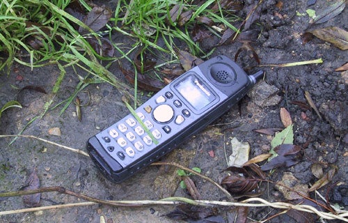 Panasonic KX-TCD290 Rugged DECT Phone lying on wet muddy ground showcasing its durability in outdoor conditions.