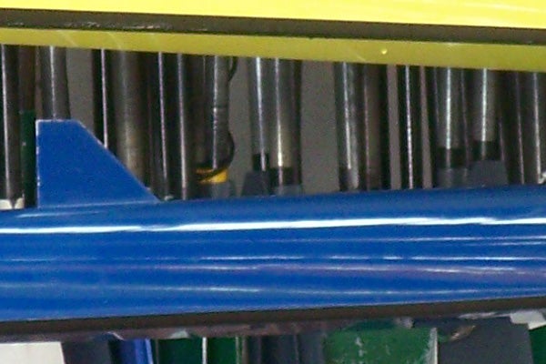 Close-up of a blue plastic component with blurred metallic cylinders in the background, unrelated to Kodak EasyShare V705 Dual Lens Camera.