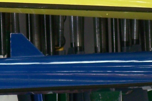 Close-up of a mechanical detail showing a blue metal part with grooves, partially obscured by yellow and green elements, potentially a macro shot demonstrating the Kodak EasyShare V705 Dual Lens Camera's close-up image capabilities.