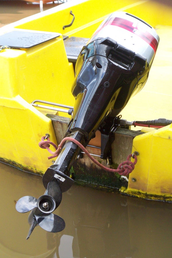 An outboard motor attached to the back of a yellow boat, with the propeller partially submerged in water.