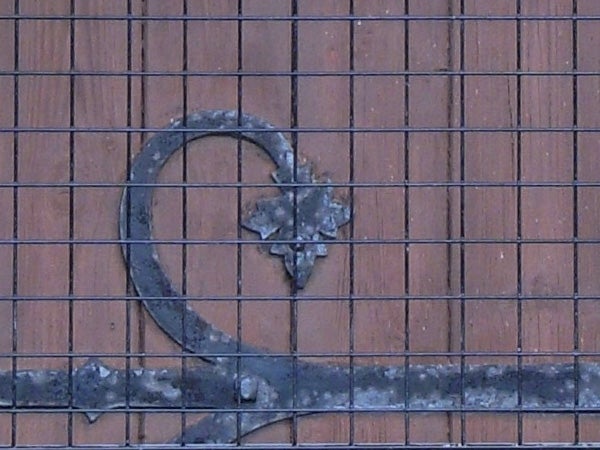 Rusted decorative metal heart attached to a wire grid in front of a brick wall.