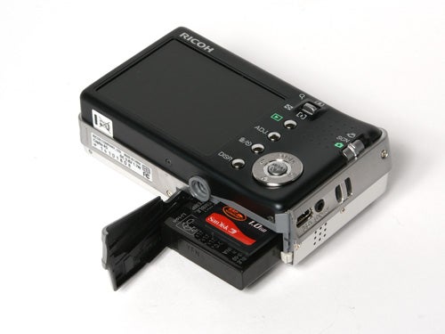 Ricoh Caplio R5 digital camera shown with its battery compartment open, displaying the battery and SD card slot on a white background.