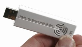 White ASUS My Cinema-U3000 Mini USB digital TV receiver held between fingers, displaying the ASUS logo and product name with a DVB logo on it.