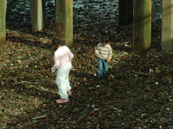 Two children playing among the stones under a pier.