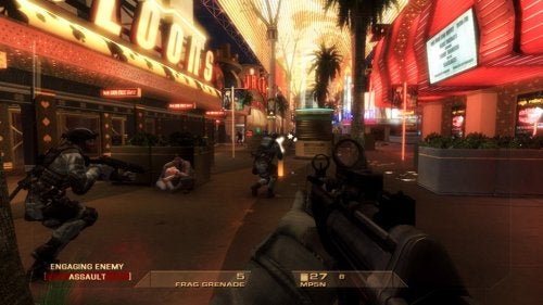Screenshot from the video game Tom Clancy's Rainbow Six: Vegas showing a first-person view where the player character is holding a submachine gun with an assault team in combat on a Las Vegas street lined with bright casino lights.