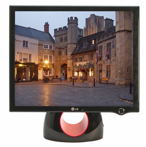 LG L1900R 'Ring' monitor with a photo on display showing a historic street scene at twilight, featuring the monitor's distinctive red circular stand and black bezel.