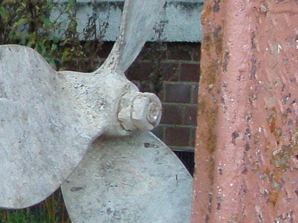 Close-up of an old, weathered boat propeller next to a brick structure with peeling paint, demonstrating the Olympus mju 1000 camera's macro photography capabilities.