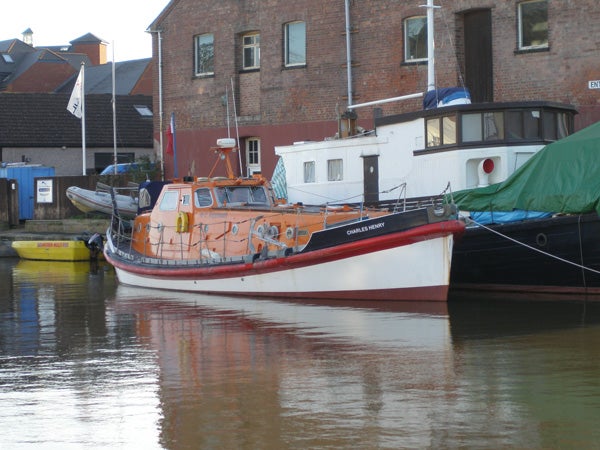 An orange and white boat moored on calm water with buildings and other boats in the background.