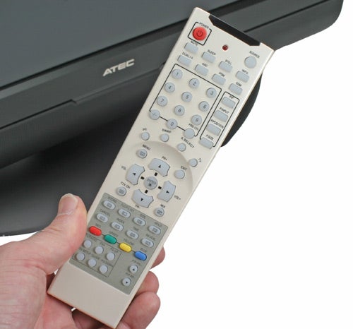 A hand holding a silver Atec remote control with multiple buttons in front of a black Atec AV371DS 37-inch LCD TV.