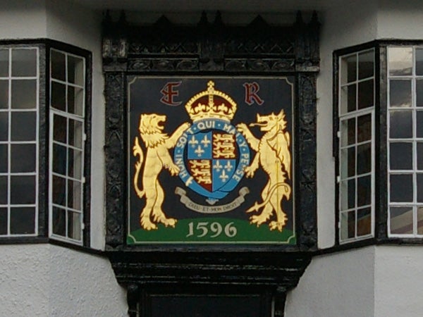 A photograph of an ornate heraldic crest featuring a lion on each side supporting a shield, with a crown at the top, set against a black background, and the date 1596 inscribed below. The image appears to be taken with a Pentax K100D Digital SLR, demonstrating the camera's detail capture in outdoor lighting conditions.
