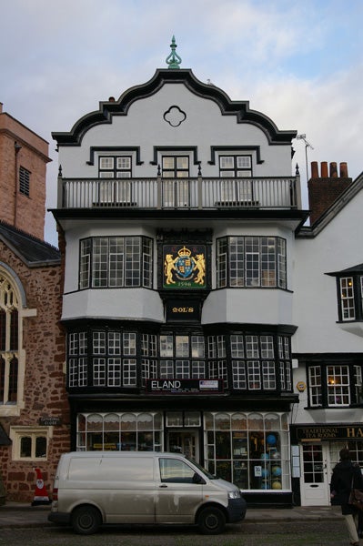 Traditional black and white half-timbered building with a decorative golden crest above the second-story windows and a parked white van in the foreground.