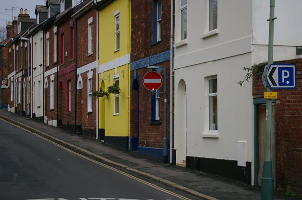 A street view photograph showing a row of colorful houses captured with the Pentax K100D Digital SLR camera, depicting its color capturing capabilities. The image displays clarity in the details of the houses, street signs, and pavement texture.