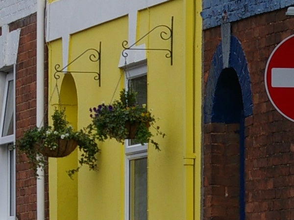 Photograph showing the textured details of a yellow building wall with windows, hanging flower baskets, and a no entry traffic sign to the right, possibly demonstrating the image quality captured by a Pentax K100D Digital SLR camera.