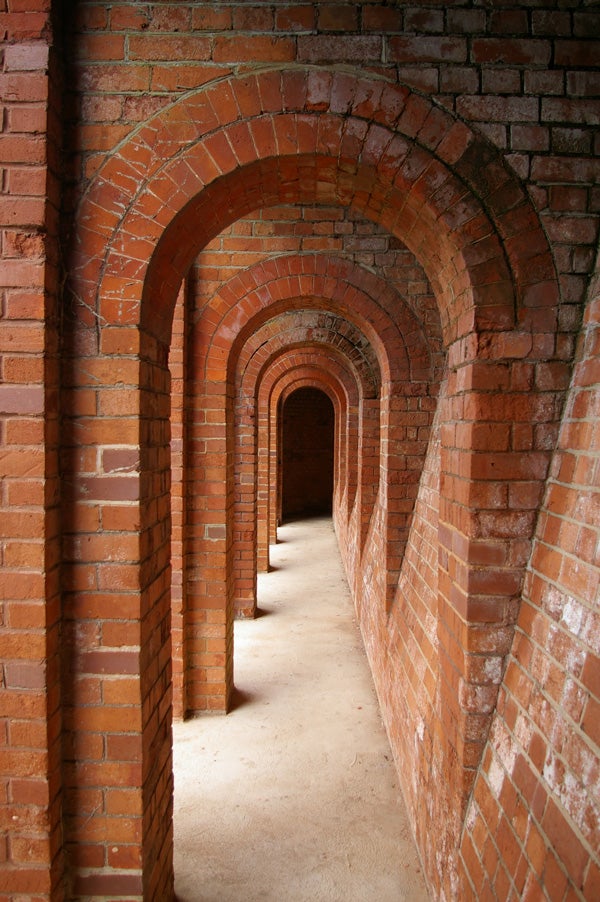 Brick archway corridor with receding arches creating a vanishing point perspective, demonstrating the depth of field and detail captured by a Pentax K100D Digital SLR camera.