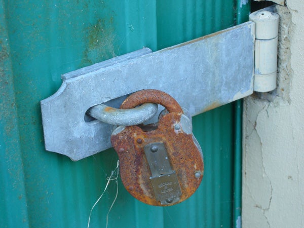 Photograph taken with a Panasonic Lumix DMC-FX01 camera showing a close-up of a rusty padlock on a metal door latch against a green corrugated surface.
