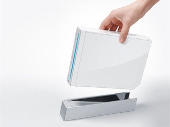 Hand placing a white Nintendo Wii console onto a gray stand on a white background.