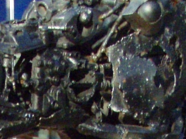 A close-up image of a heavily textured and possibly metallic surface with indistinct shapes, potentially showcasing the Olympus mju 725 SW camera's macro photography capabilities.