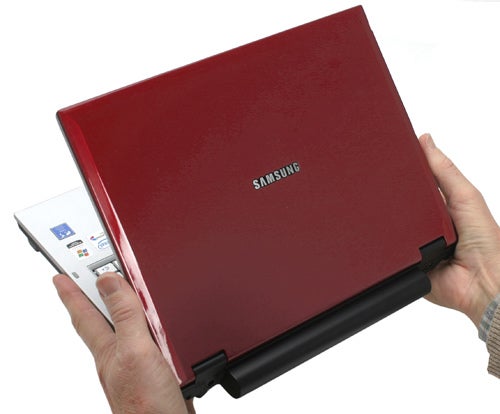 Person holding a red Samsung Q35 laptop showing the brand logo and part of the laptop's ports and power indicator.