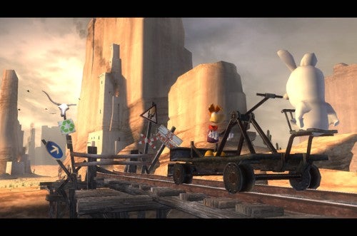 A scene from Rayman Raving Rabbids video game showing a character in a gladiator costume being chased by a large white rabbid on a wooden cart with a catapult on a desert track with rock pillars in the background.