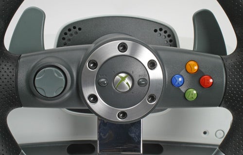 Close-up view of a Microsoft Xbox 360 Wireless Steering Wheel with face buttons and logo, mounted on a stand.
