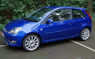 Blue compact car parked with focus on the driver's side, potentially to illustrate a vehicle where the Parrot MK600 Bluetooth car kit could be installed.