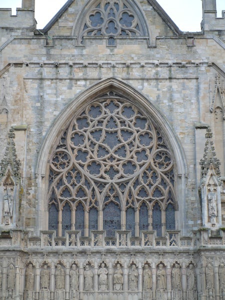 A detailed photograph of an ornate gothic church window with intricate stone tracery and statues set into niches on the facade, captured with a Panasonic DMC-L1 Digital SLR camera.