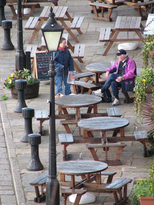 Photograph demonstrating the zoom capabilities of the Canon PowerShot S3 IS, showing two people seated at wooden benches in an outdoor seating area, taken from an elevated angle with a clear focus and high level of detail.