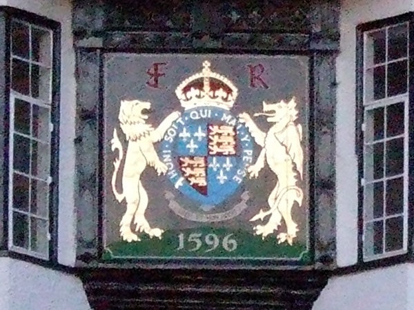 Close-up photo of a heraldic shield with a crown on top flanked by two lions, featuring a motto and the date 1596, displayed on a building's exterior.