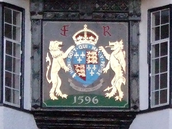 A close-up photo of an ornate coat of arms, featuring a shield with a detailed design flanked by two standing lions, against a dark background, with the date 1596 inscribed below, demonstrating the zoom capabilities and image quality of the Fujifilm FinePix S9600 camera.