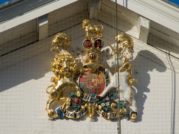 Golden coat of arms emblem on a white wall.